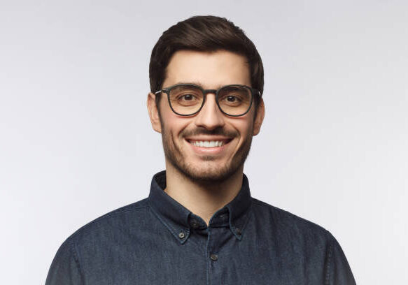 Headshot of cheerful handsome man with trendy haircut and eyeglasses isolated on gray background